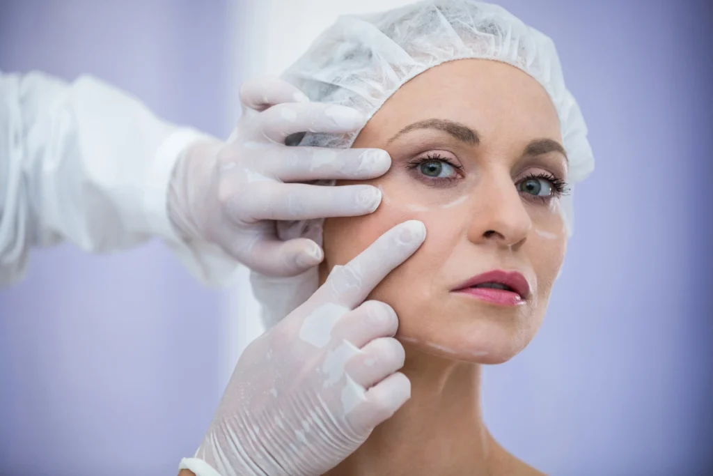 Face Surgery in Dubai: 7 Popular Procedures That Can Enhance Facial Balance 2 A plastic surgeon wearing white gloves carefully evaluating a woman's upper cheek and under-eye area during a consultation for facelift or blepharoplasty surgery.